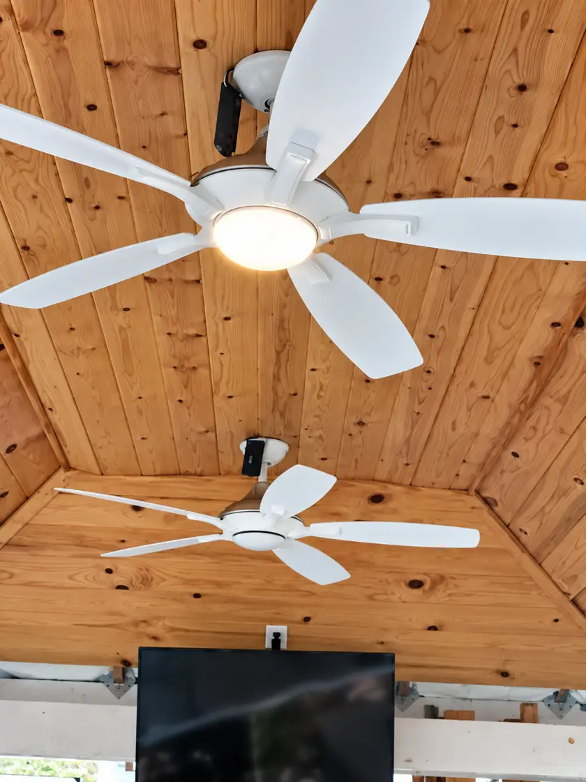 Two ceiling fans with lights on a covered wood patio